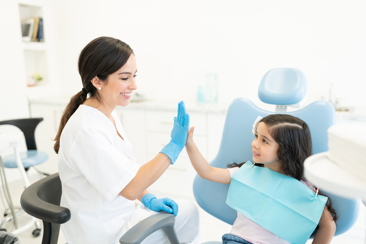 Cute Hispanic girl high-fiving with female dentist during checkup at dental clinic
