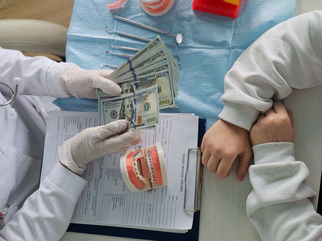 Dentist keeps money orthodontic model of braces. Consultation of orthodontist installation of braces for teenagers and cost