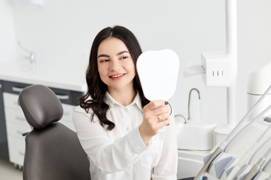 Happy woman patient checking teeth in mirror.